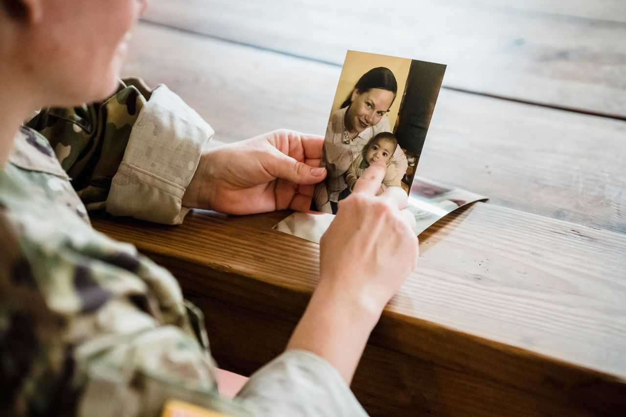 A soldier in uniform reminiscing while holding a photograph of family members.